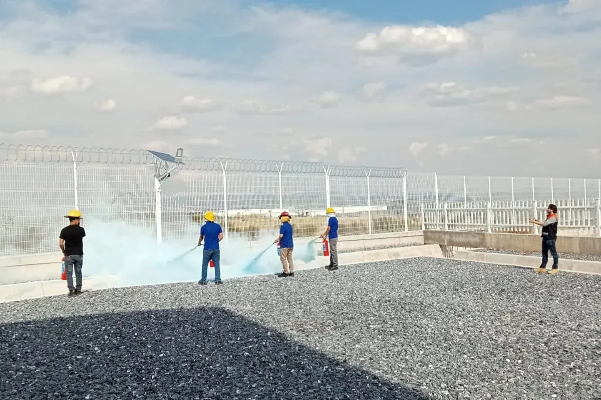 Participantes con casco descargan extintores de polvo químico seco en un patio de práctica mientras el instructor observa