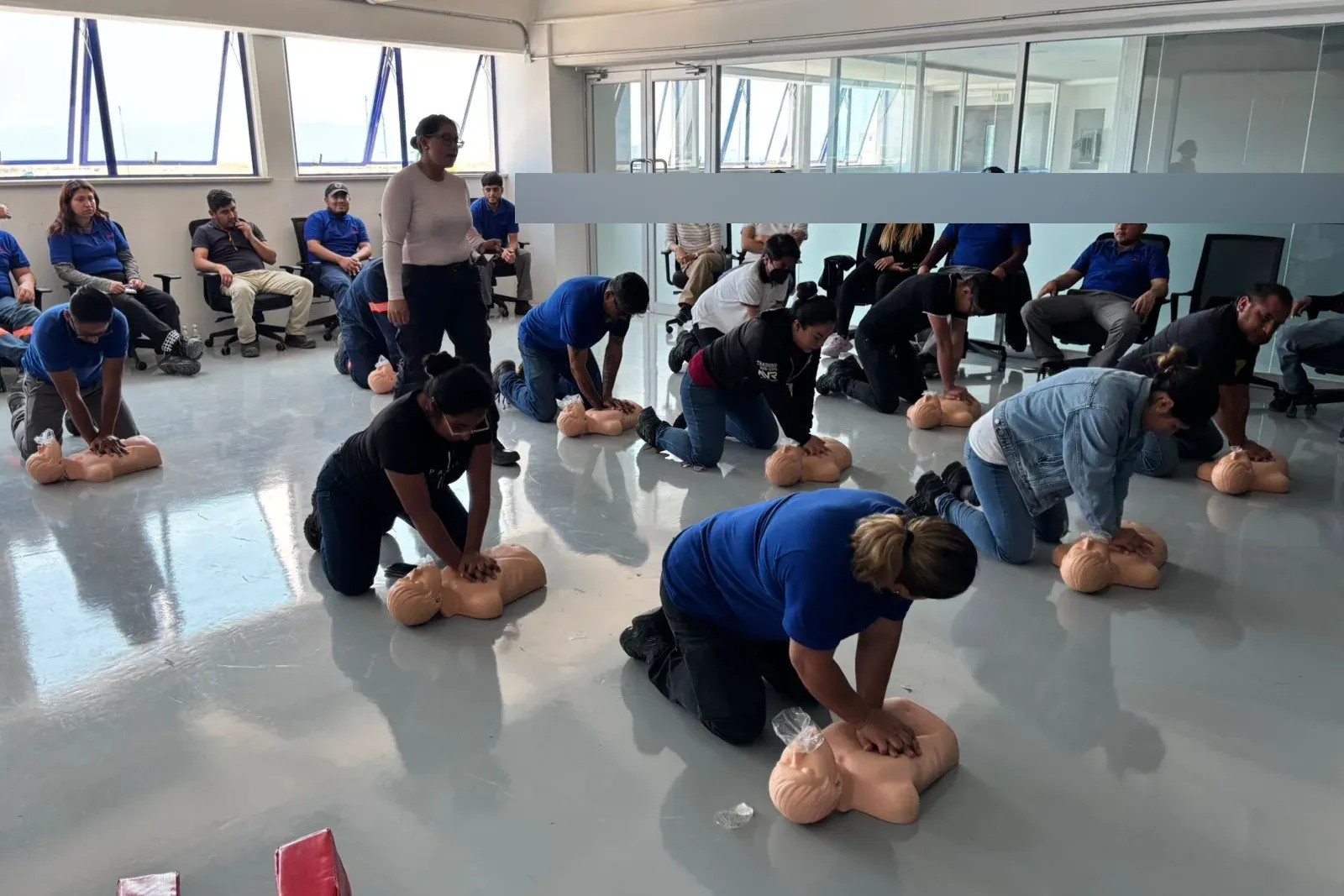 Instructora supervisa a varios participantes que practican compresiones torácicas sobre maniquíes