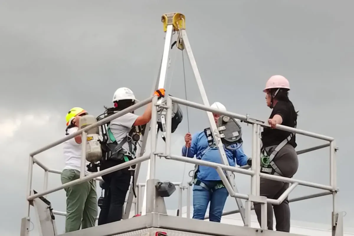 Rescatistas con arnés, casco y equipo de respiración autónomo preparan una maniobra junto al trípode en una plataforma elevada
