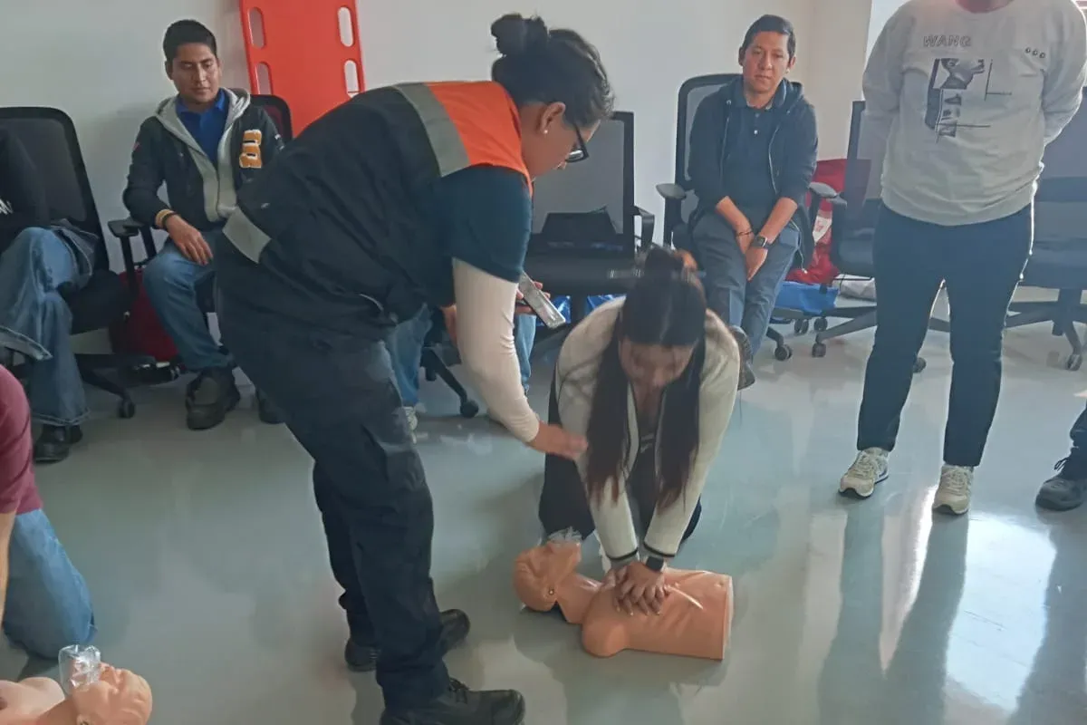 Instructora corrige la posición de las manos de una participante que practica RCP sobre un maniquí