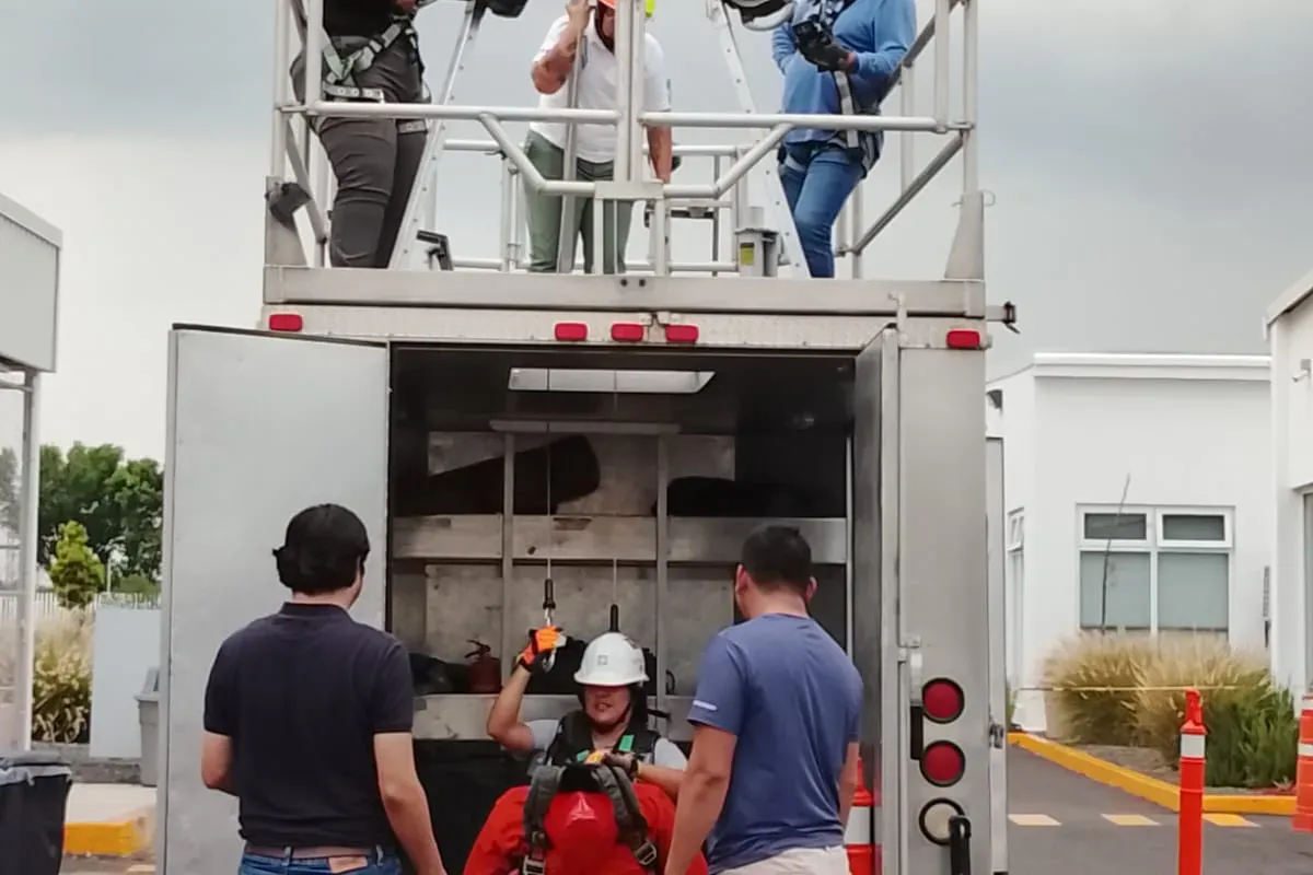 Instructores supervisan la extracción de un maniquí con arnés desde un simulador de espacio confinado con trípode y malacate