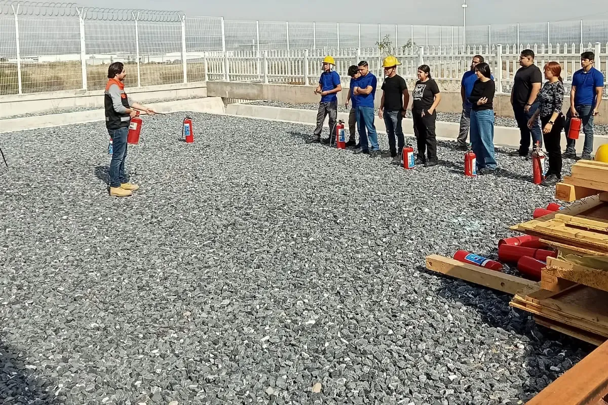 Instructor explica el uso del extintor a una fila de participantes con un extintor cada uno