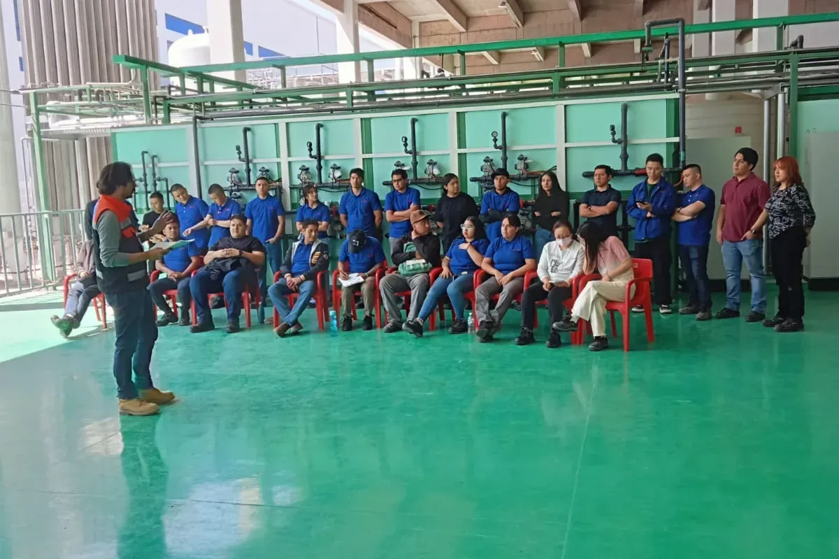 Instructor con chaleco y hojas en mano imparte una sesión a un grupo numeroso de brigadistas en una planta