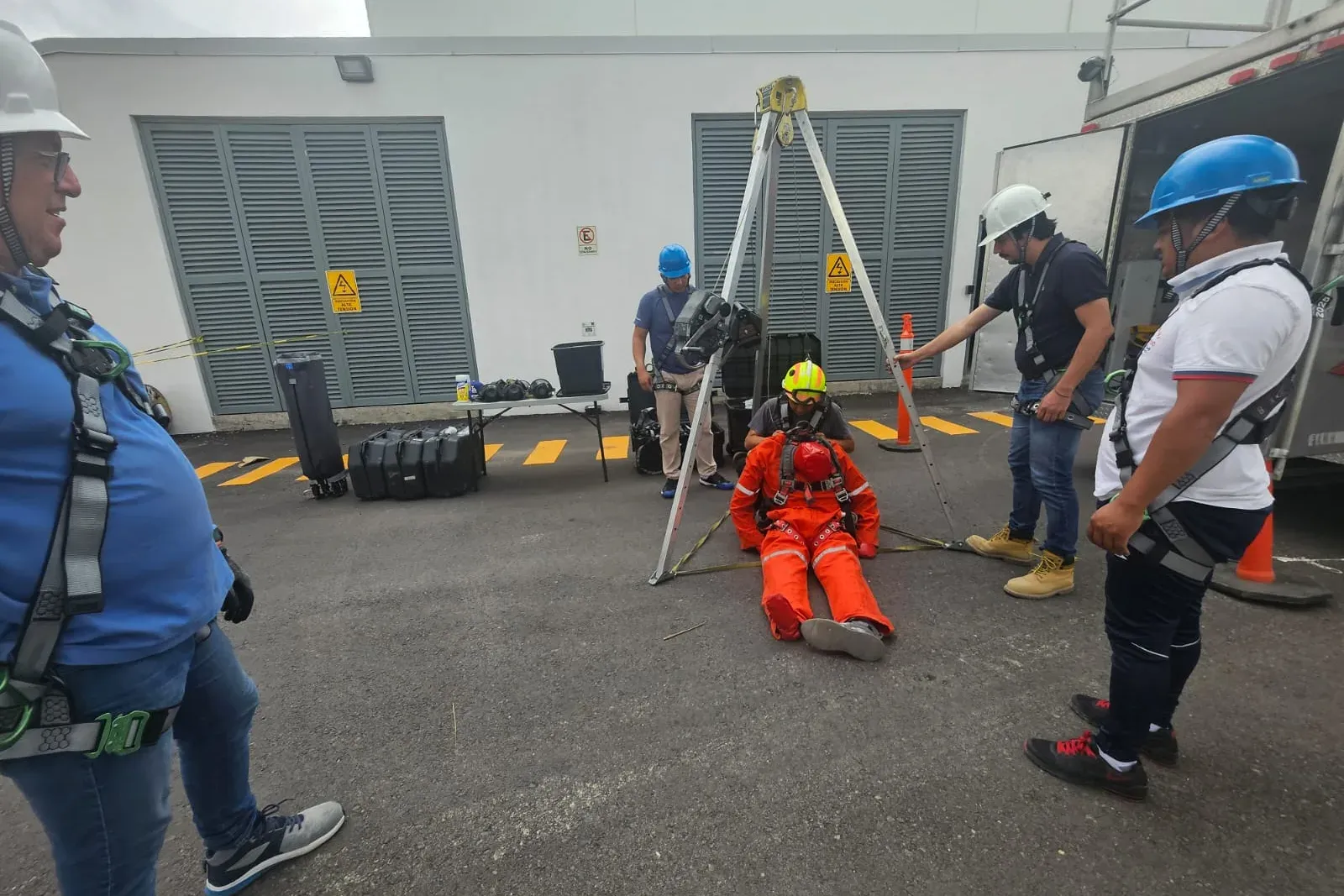 Rescatista con casco atiende a un maniquí con arnés bajo un trípode mientras los instructores observan
